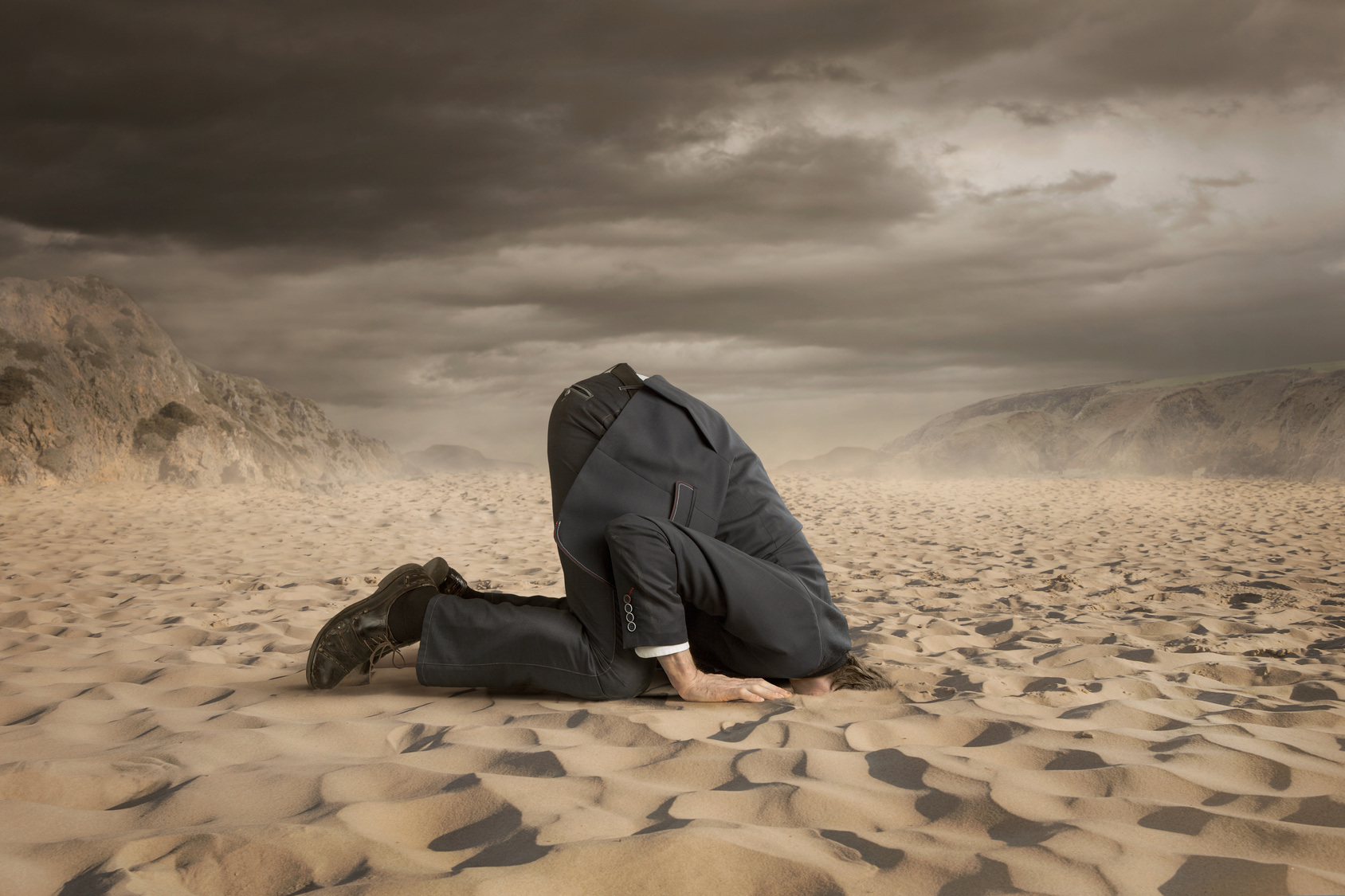 Young businessman hiding head in the sand